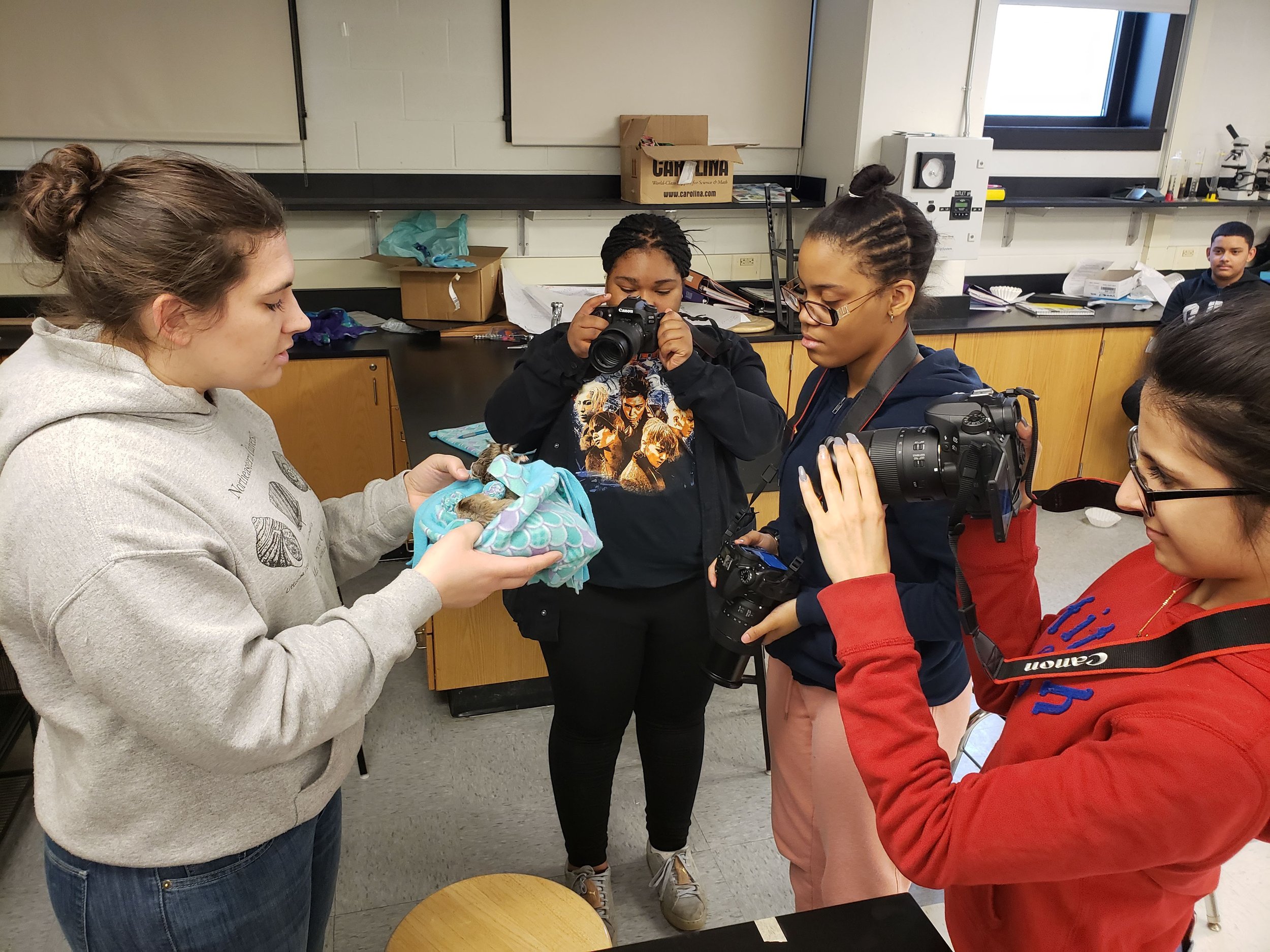 Three students with cameras and a teacher in a classroom